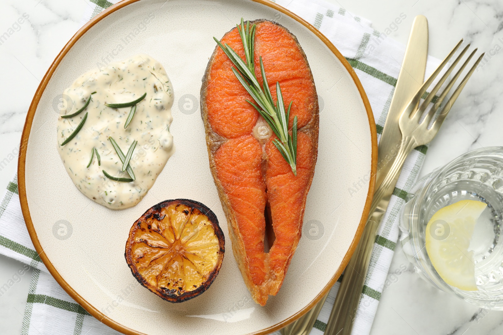 Seafood. Tasty salmon steak served with sauce, rosemary and lemon on white marble table, flat lay Photo of Seafood. Tasty salmon steak served with sauce, rosemary and lemon on white marble table, flat lay