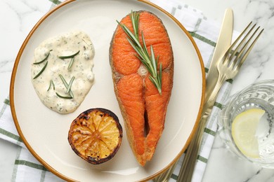 Photo of Seafood. Tasty salmon steak served with sauce, rosemary and lemon on white marble table, flat lay