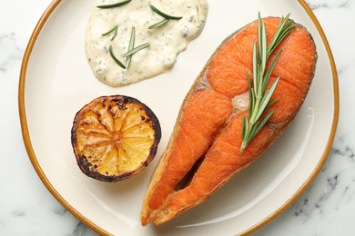 Photo of Seafood. Tasty salmon steak served with sauce, rosemary and lemon on white marble table, top view