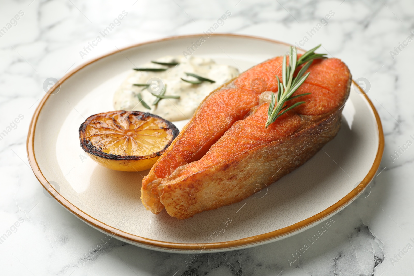 Seafood. Tasty salmon steak served with sauce, rosemary and lemon on white marble table, closeup Photo of Seafood. Tasty salmon steak served with sauce, rosemary and lemon on white marble table, closeup