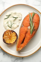 Photo of Seafood. Tasty salmon steak served with sauce, rosemary and lemon on white marble table, top view