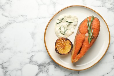 Photo of Seafood. Tasty salmon steak served with sauce, rosemary and lemon on white marble table, top view. Space for text