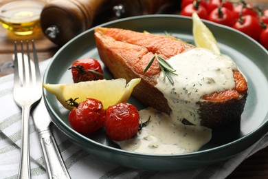Photo of Seafood. Tasty salmon steak served with sauce, tomatoes, rosemary and lemon on table, closeup