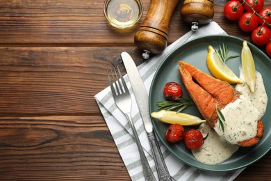 Photo of Seafood. Tasty salmon steak served with sauce, tomatoes, rosemary and lemon on wooden table, flat lay. Space for text