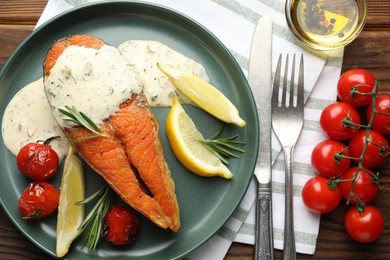 Photo of Seafood. Tasty salmon steak served with sauce, tomatoes, rosemary and lemon on wooden table, flat lay
