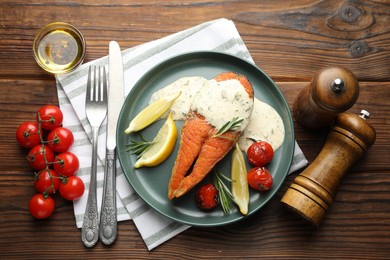 Photo of Seafood. Tasty salmon steak served with sauce, tomatoes, rosemary and lemon on wooden table, flat lay