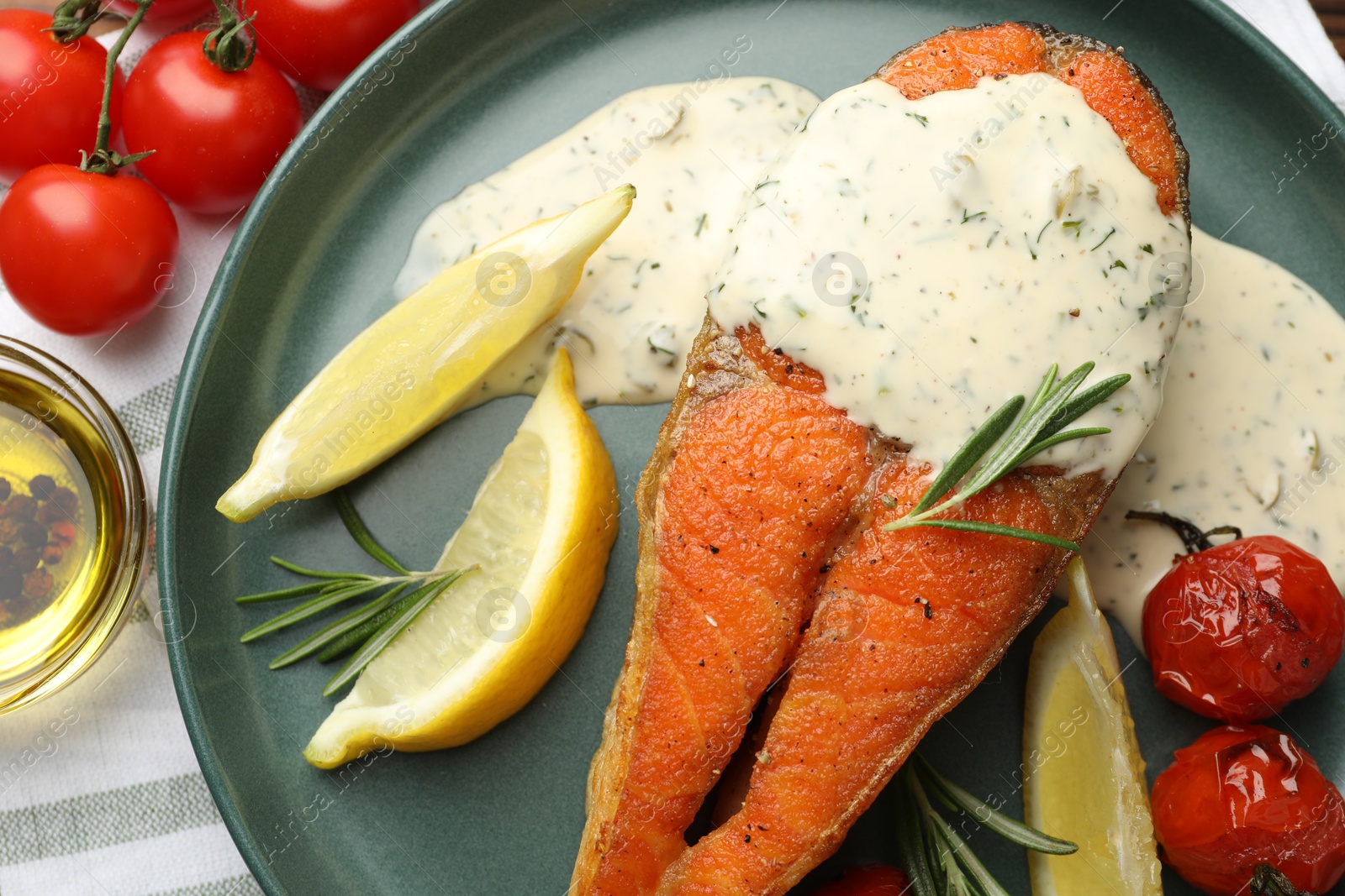 Seafood. Tasty salmon steak served with sauce, tomatoes, rosemary and lemon on table, flat lay Photo of Seafood. Tasty salmon steak served with sauce, tomatoes, rosemary and lemon on table, flat lay