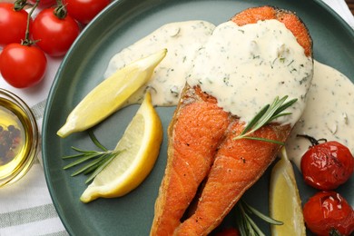 Photo of Seafood. Tasty salmon steak served with sauce, tomatoes, rosemary and lemon on table, flat lay