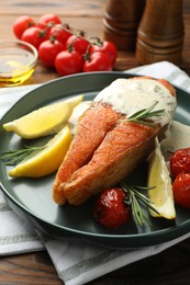 Photo of Seafood. Tasty salmon steak served with sauce, tomatoes, rosemary and lemon on wooden table, closeup
