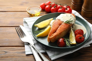 Photo of Seafood. Tasty salmon steak served with sauce, tomatoes, rosemary and lemon on wooden table, closeup