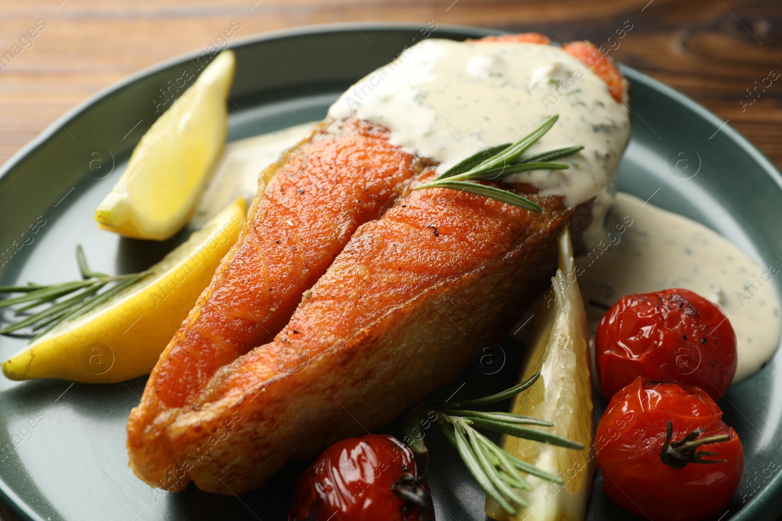 Seafood. Tasty salmon steak served with sauce, tomatoes, rosemary and lemon on table, closeup Photo of Seafood. Tasty salmon steak served with sauce, tomatoes, rosemary and lemon on table, closeup