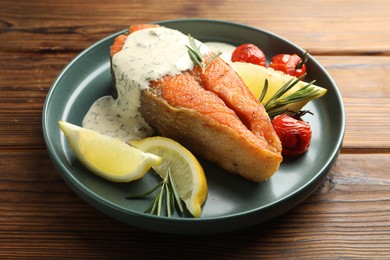 Photo of Seafood. Tasty salmon steak served with sauce, tomatoes, rosemary and lemon on wooden table, closeup