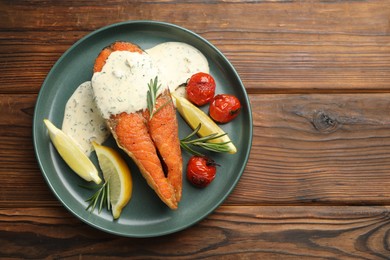 Photo of Seafood. Tasty salmon steak served with sauce, tomatoes, rosemary and lemon on wooden table, top view. Space for text