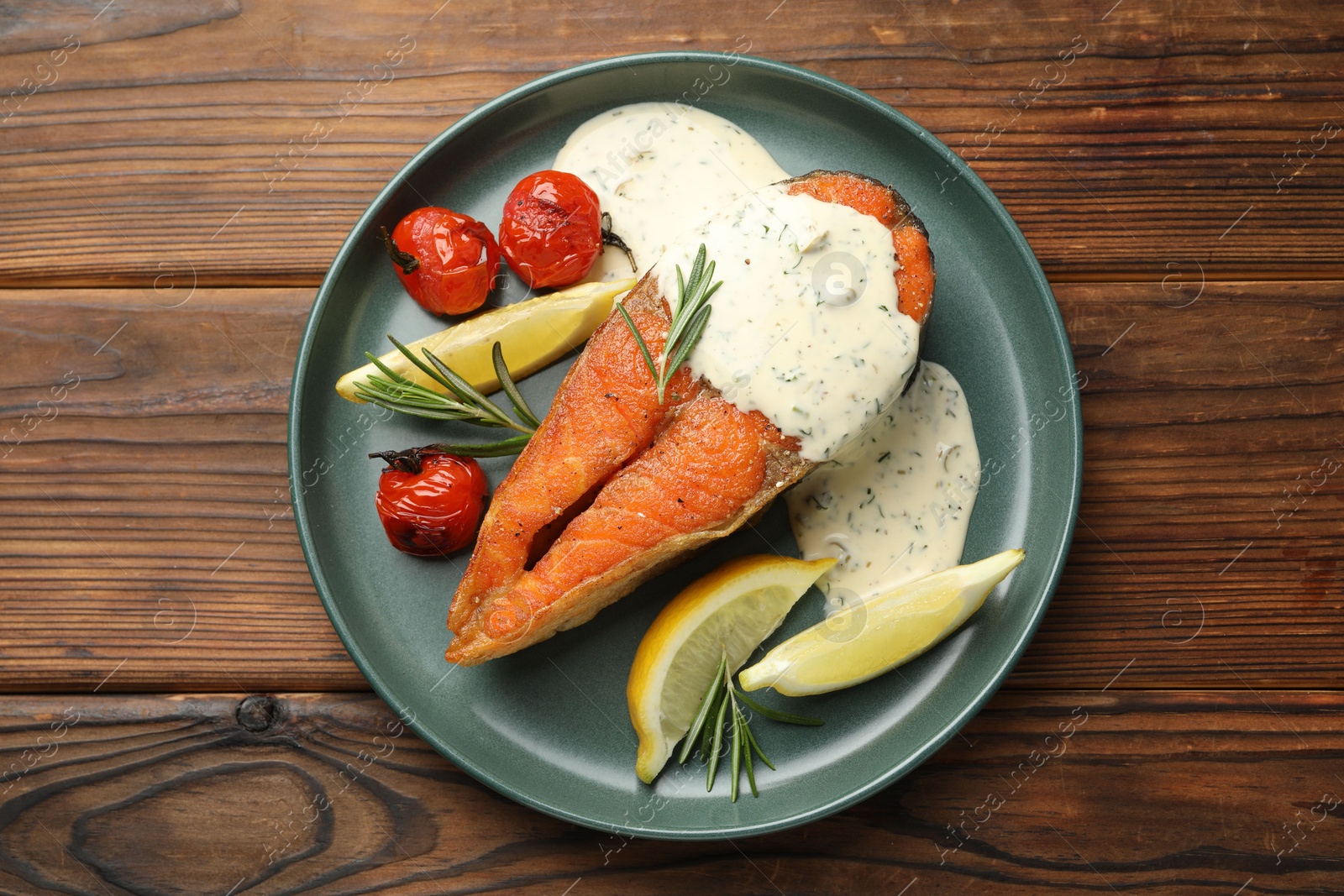 Seafood. Tasty salmon steak served with sauce, tomatoes, rosemary and lemon on wooden table, top view Photo of Seafood. Tasty salmon steak served with sauce, tomatoes, rosemary and lemon on wooden table, top view