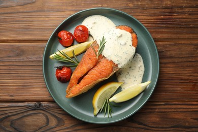 Photo of Seafood. Tasty salmon steak served with sauce, tomatoes, rosemary and lemon on wooden table, top view