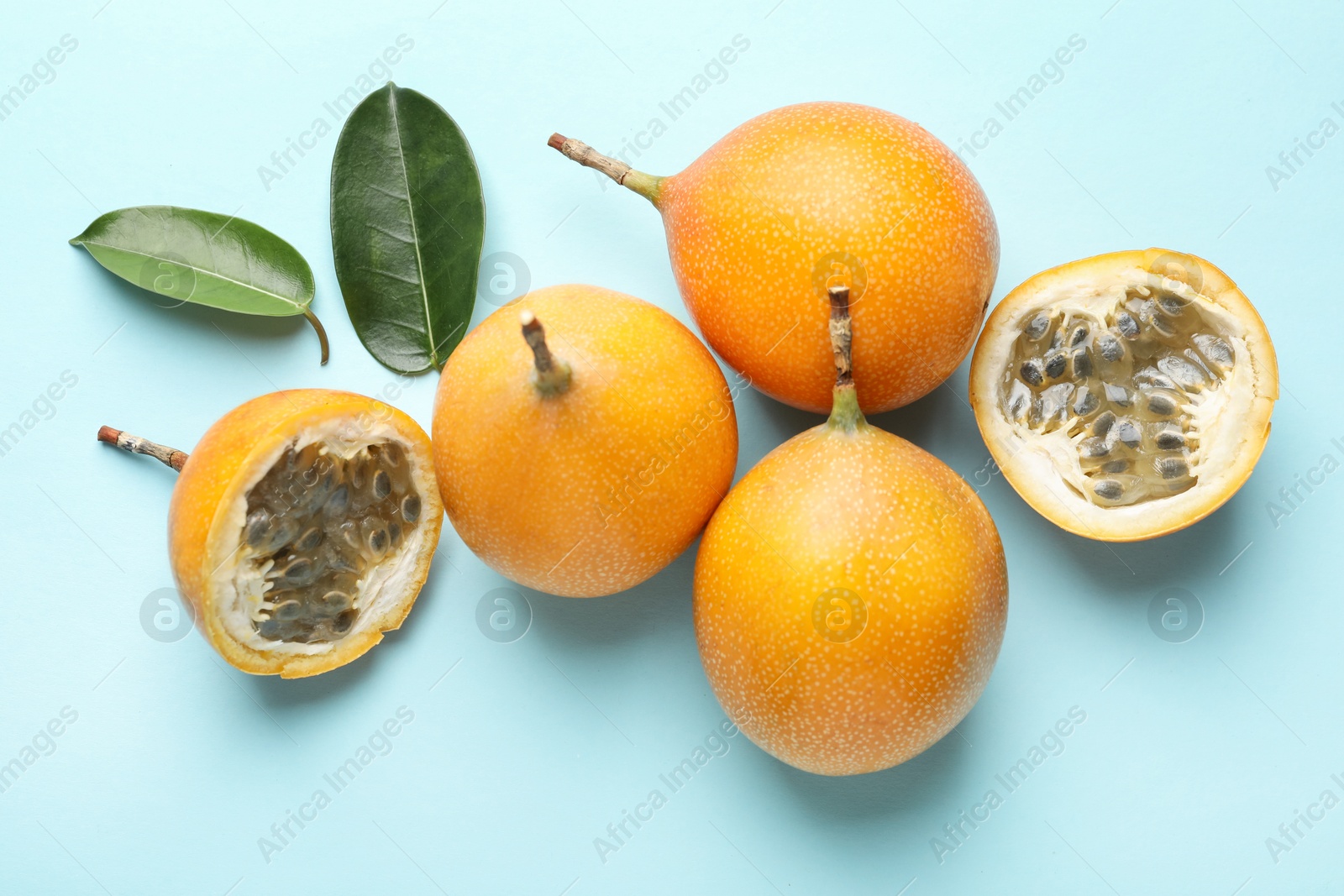 Ripe yellow passion fruits and leaves on light blue background, flat lay Photo of Ripe yellow passion fruits and leaves on light blue background, flat lay