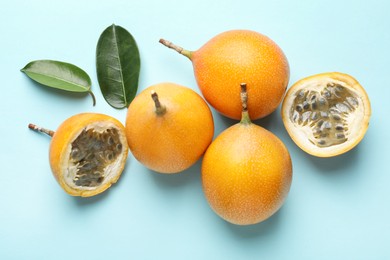 Photo of Ripe yellow passion fruits and leaves on light blue background, flat lay