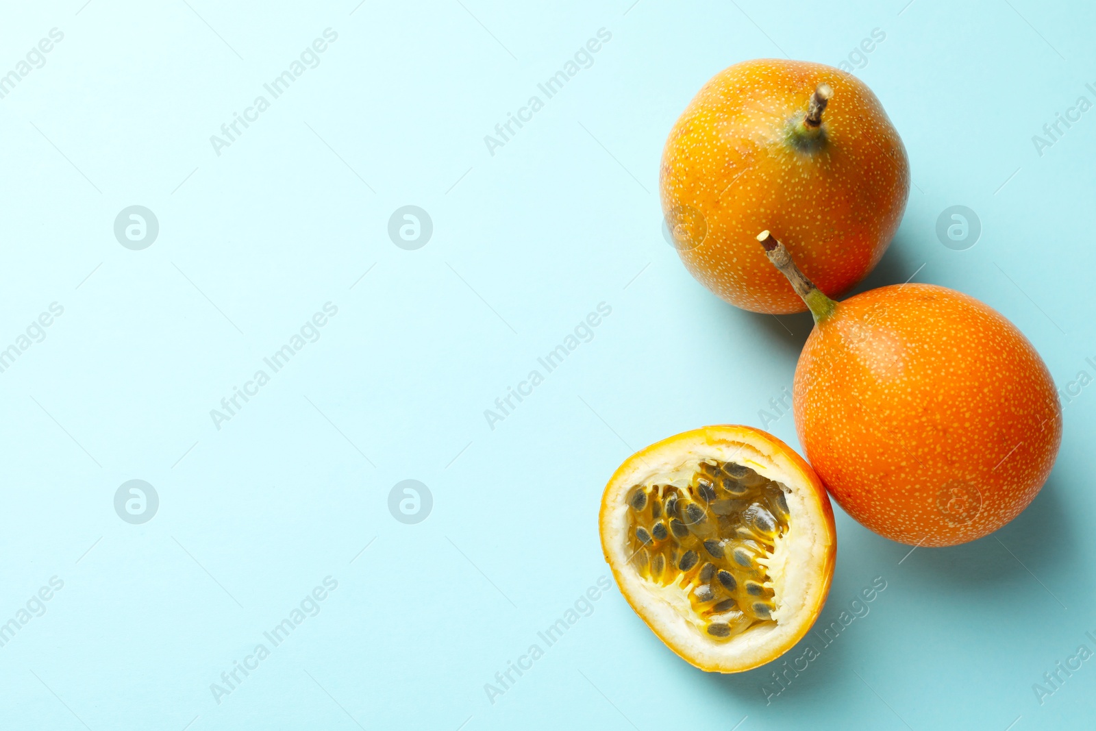 Photo of Ripe yellow passion fruits on light blue background, flat lay. Space for text