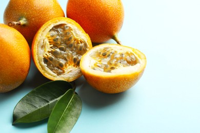 Photo of Ripe yellow passion fruits and leaves on light blue background, closeup