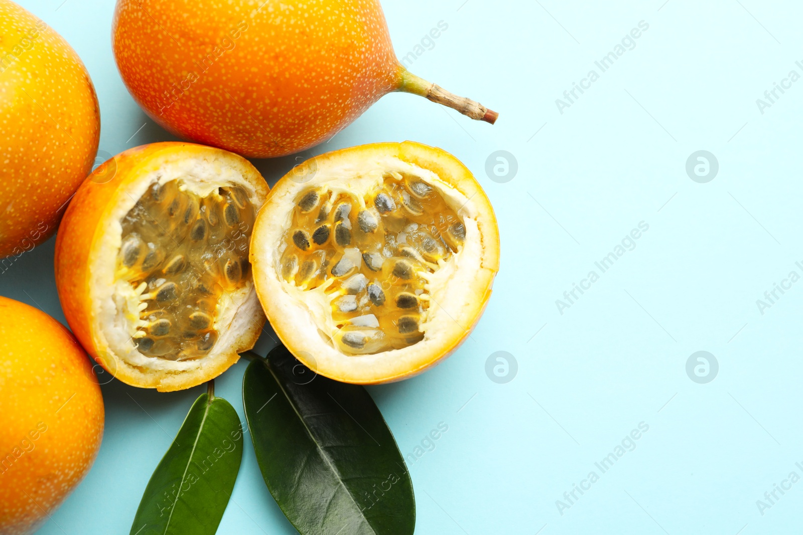 Photo of Ripe yellow passion fruits and leaves on light blue background, flat lay. Space for text