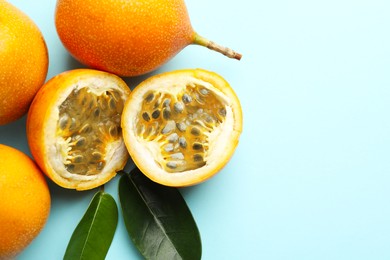 Photo of Ripe yellow passion fruits and leaves on light blue background, flat lay. Space for text