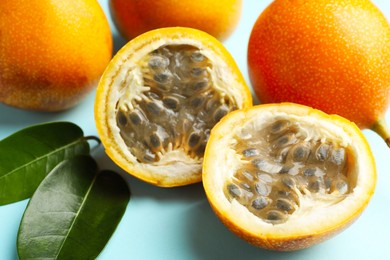 Photo of Ripe yellow passion fruits and leaves on light blue background, closeup