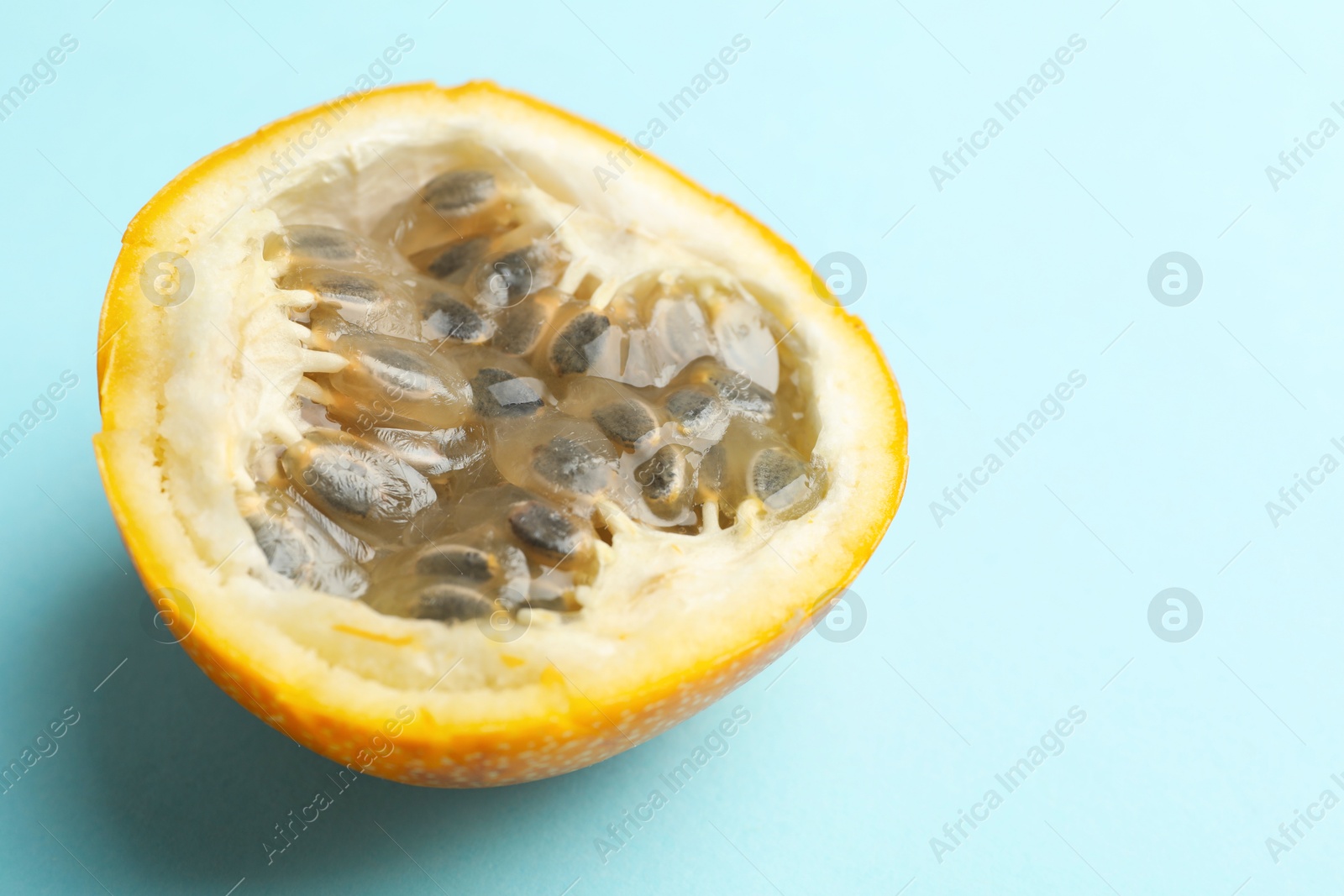 Piece of ripe yellow passion fruit on light blue background, closeup. Space for text Photo of Piece of ripe yellow passion fruit on light blue background, closeup. Space for text