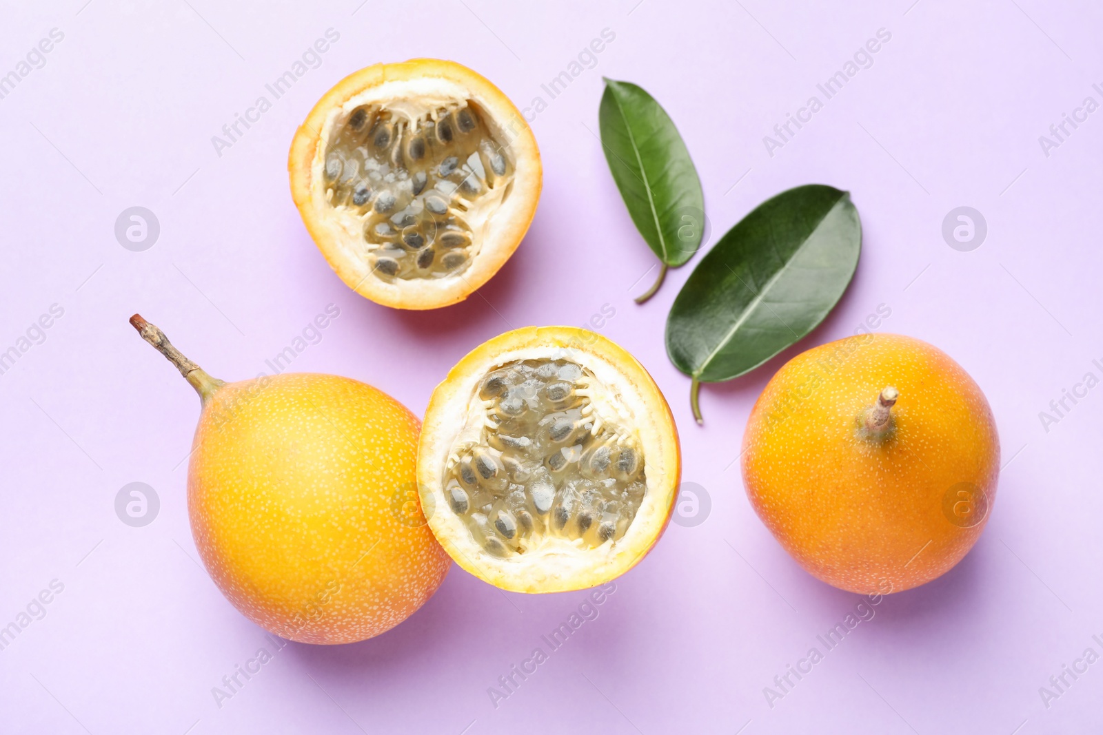 Ripe yellow passion fruits and leaves on lilac background, flat lay Photo of Ripe yellow passion fruits and leaves on lilac background, flat lay