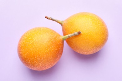 Photo of Ripe yellow passion fruits on lilac background, flat lay