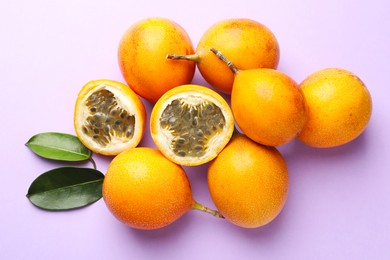 Photo of Ripe yellow passion fruits and leaves on lilac background, flat lay