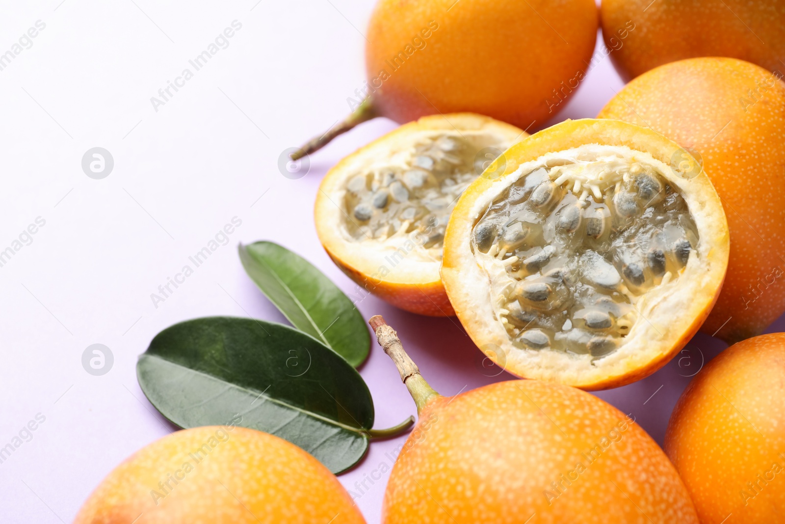 Photo of Ripe yellow passion fruits and leaves on lilac background, closeup. Space for text