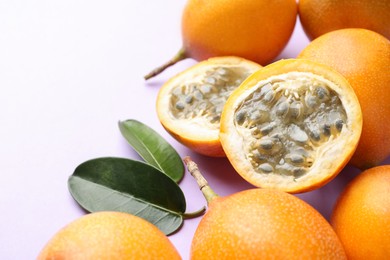 Photo of Ripe yellow passion fruits and leaves on lilac background, closeup. Space for text