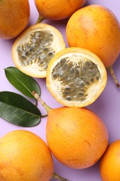 Photo of Ripe yellow passion fruits and leaves on lilac background, flat lay