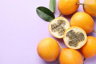 Photo of Ripe yellow passion fruits and leaves on lilac background, flat lay. Space for text