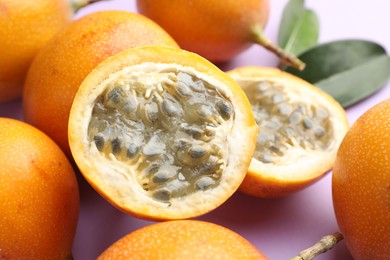 Photo of Ripe yellow passion fruits and leaves on lilac background, closeup