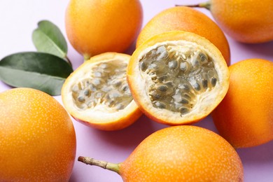 Photo of Ripe yellow passion fruits and leaves on lilac background, closeup
