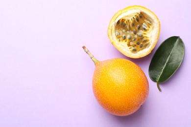 Photo of Ripe yellow passion fruits and leaf on lilac background, flat lay. Space for text