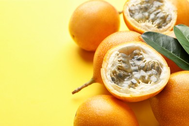 Photo of Ripe passion fruits and leaves on yellow background, closeup. Space for text