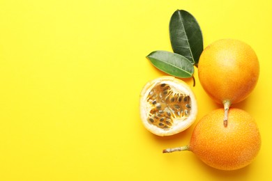 Photo of Ripe passion fruits and leaves on yellow background, flat lay. Space for text