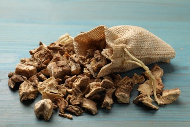 Photo of Pieces of dry chicory roots and sack on blue wooden table, closeup