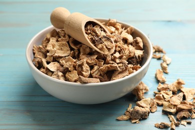 Photo of Pieces of dry chicory roots and scoop in bowl on blue wooden table, closeup