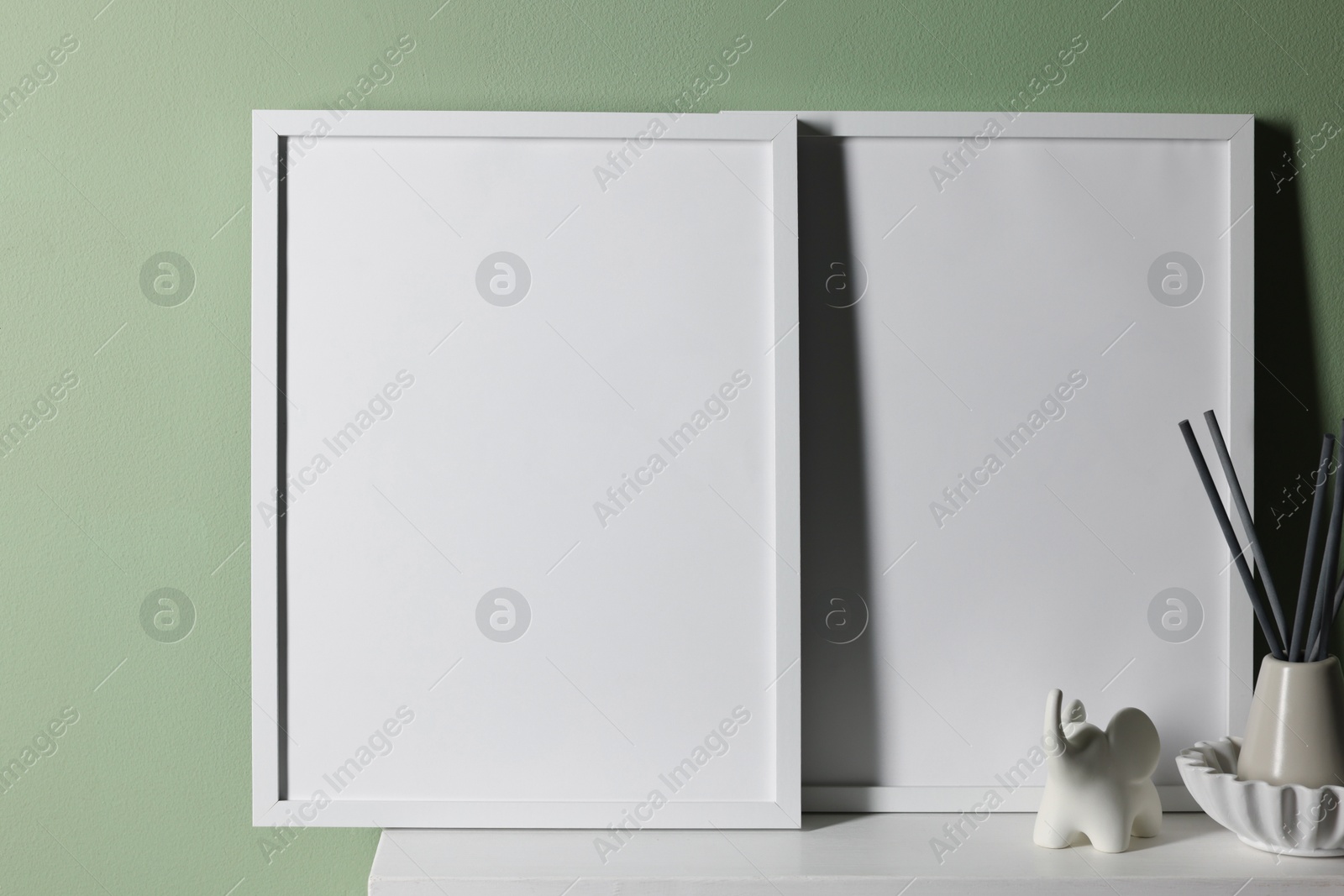 Empty picture frames and other decor on white shelf near pale green wall indoors Photo of Empty picture frames and other decor on white shelf near pale green wall indoors