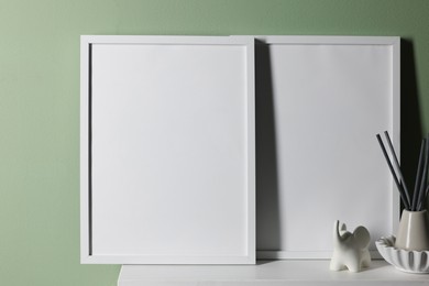 Photo of Empty picture frames and other decor on white shelf near pale green wall indoors