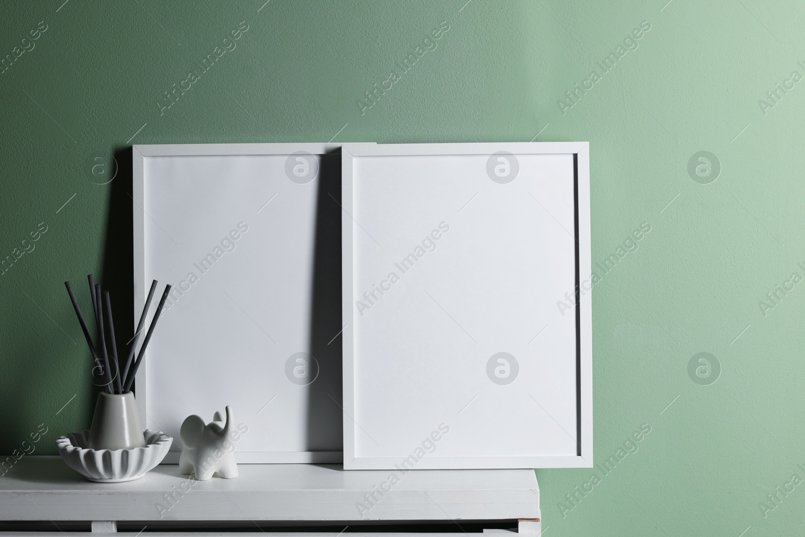 Empty picture frames and other decor on white shelf near pale green wall indoors Photo of Empty picture frames and other decor on white shelf near pale green wall indoors