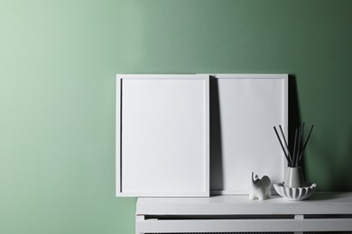 Photo of Empty picture frames and other decor on white shelf near pale green wall indoors, space for text