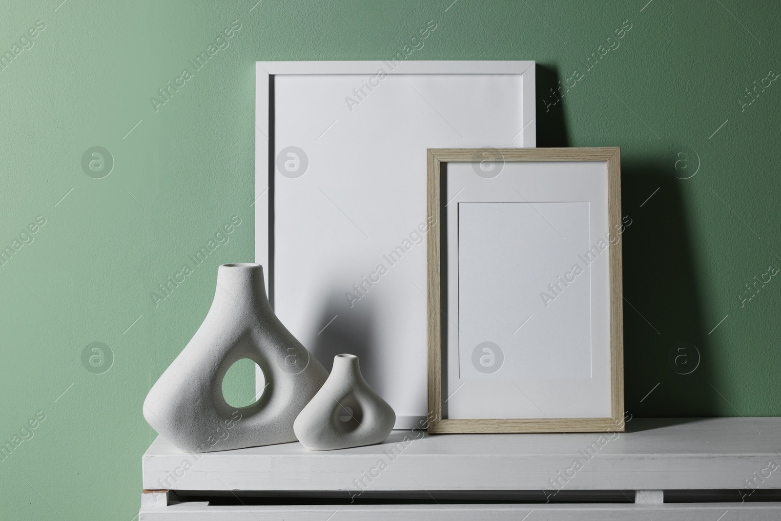 Empty picture frames and other decor on white shelf near pale green wall indoors Photo of Empty picture frames and other decor on white shelf near pale green wall indoors