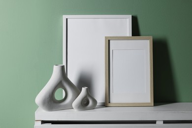 Photo of Empty picture frames and other decor on white shelf near pale green wall indoors