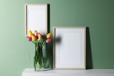 Photo of Empty picture frames and beautiful tulips indoors