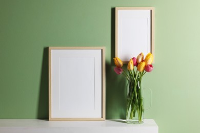 Photo of Empty picture frames and beautiful tulips indoors