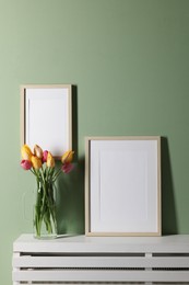 Photo of Empty picture frames and beautiful tulips indoors